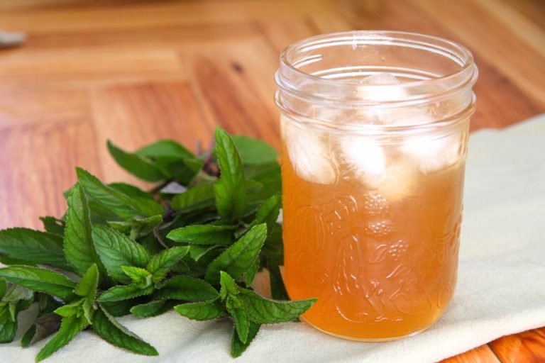 A jar on a wooden courter top, filled with ice and chilled mint tea