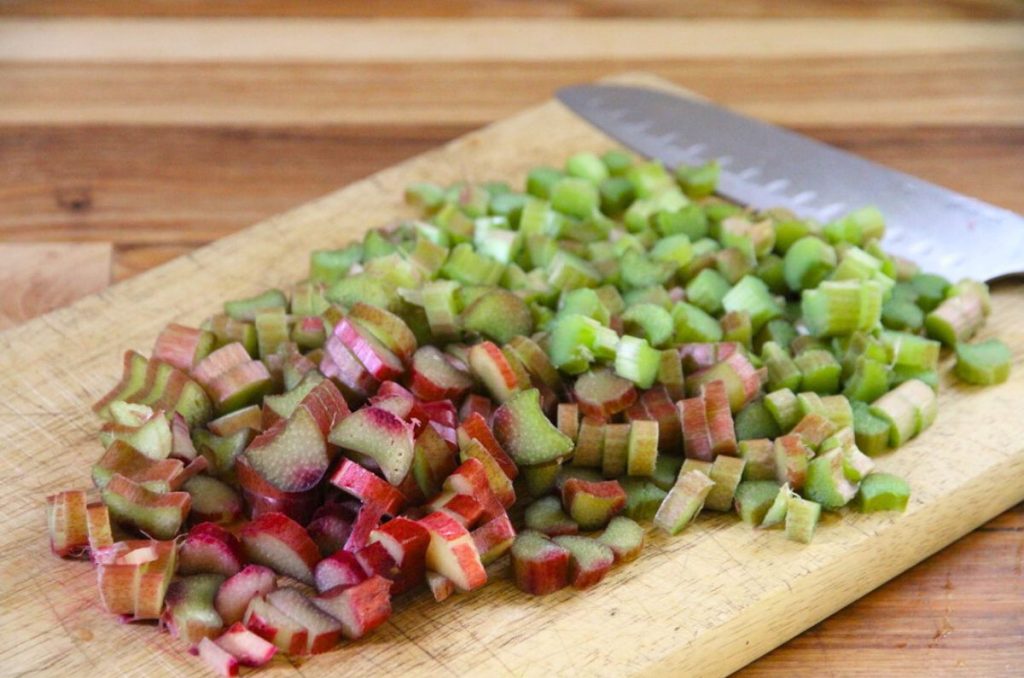 A wooden cutting board filled with rhubarb slices that are 1/2 to 1/4 inch thick.