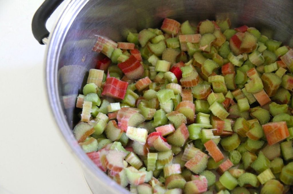 Slices of raw rhubarb in a large sauce pan on the stove, ready for cooking.