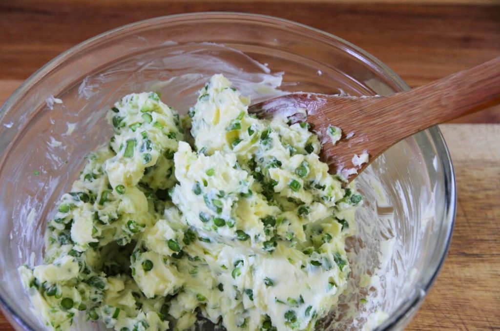 Mixing butter and minced garlic scapes together with a wooden spoon.