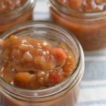 A jar of golden red rhubarb freezer jam with a spoon.