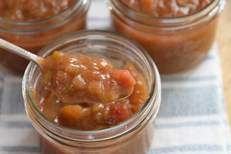 A jar of golden red rhubarb freezer jam with a spoon.