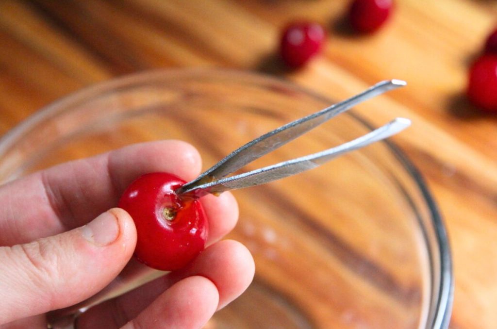 Using the back of tweezers to scoop out sour cherry pits.