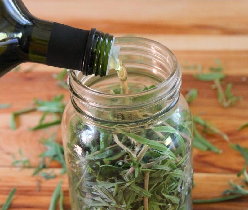 Pouring oil into a mason jar stuffed with fresh lavender buds and green leaves.