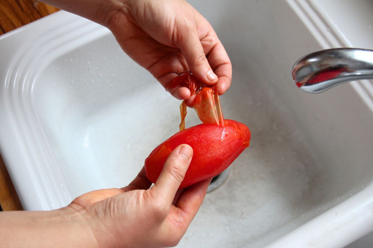 Peeling a frozen tomato after running it under hot water to loosen the peel. 
