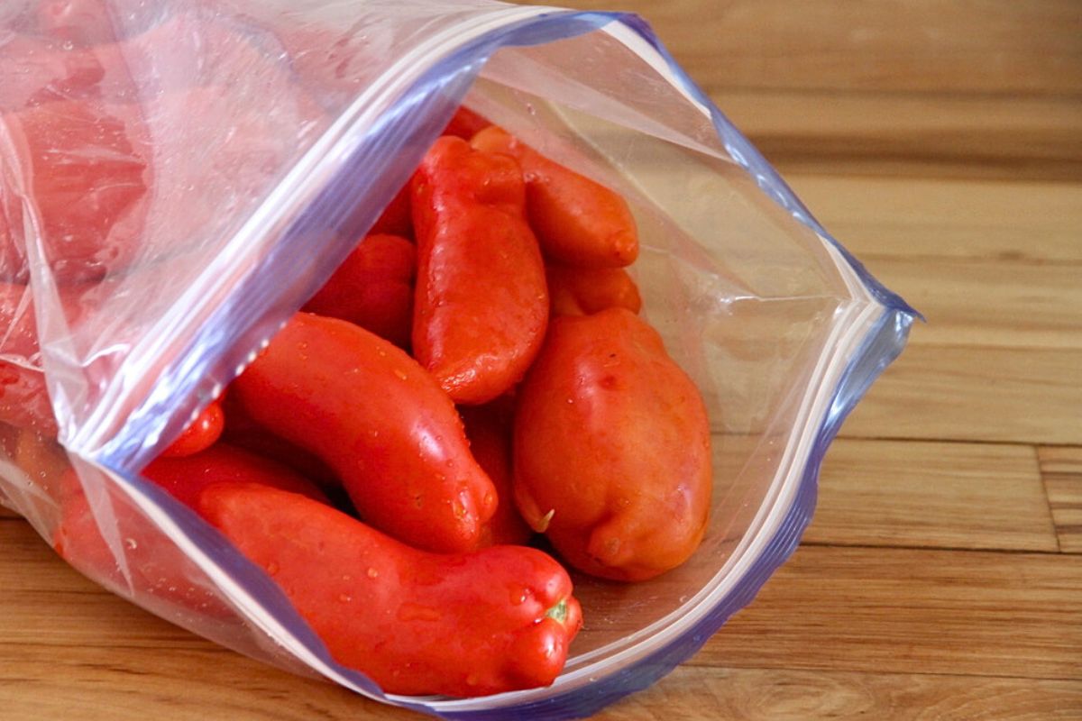 A plastic freezer bag with a zip lock, filled with tomatoes for freezing.