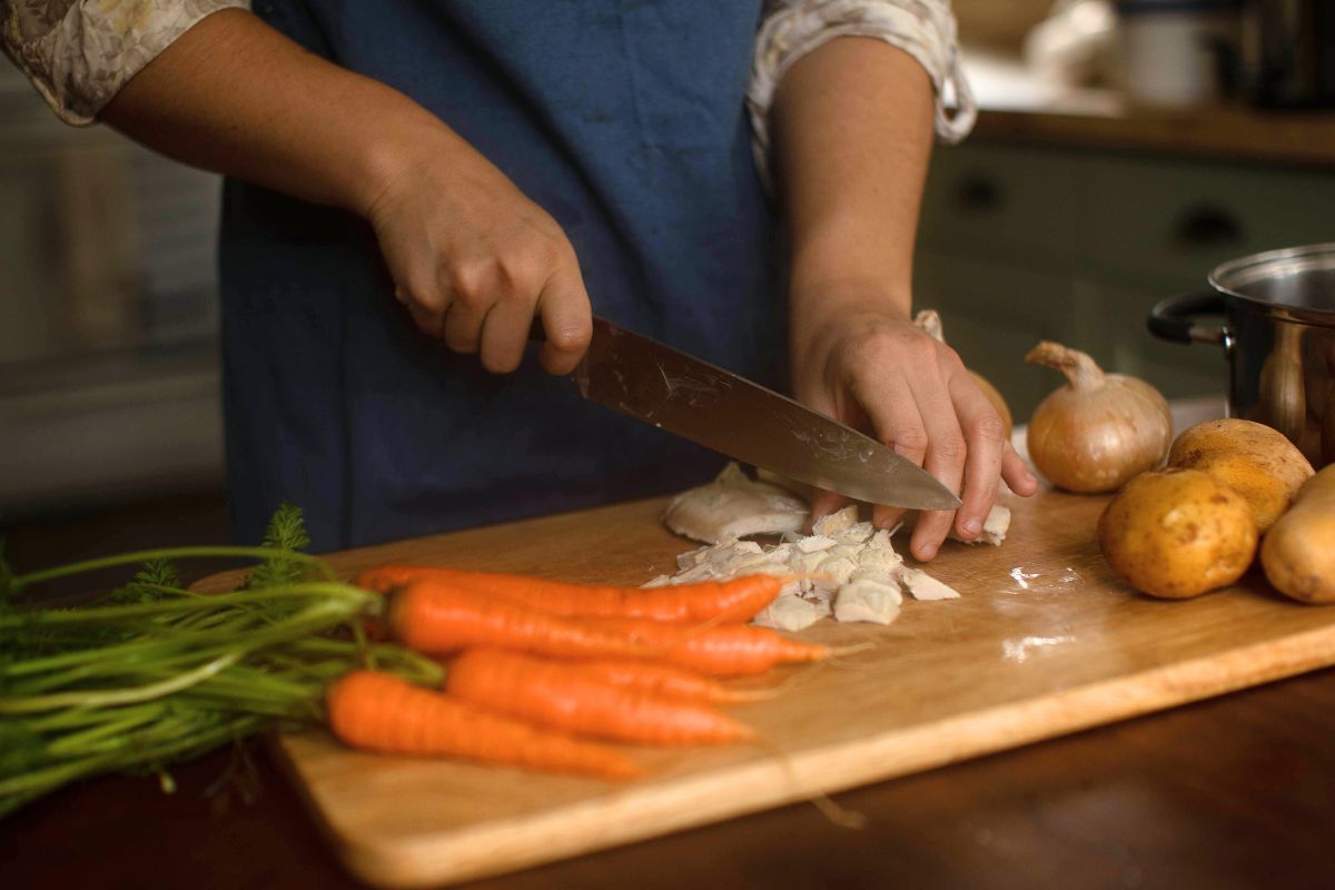 Carrots, potatoes and chicken meat on a wooden cutting board.