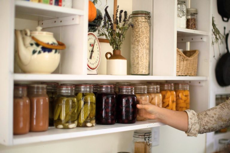 A row of canned food sitting on a white kitchen shelf.