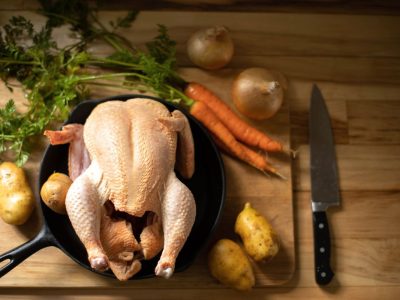 A whole chicken in a cast iron skillet, surrounded by vegetables.