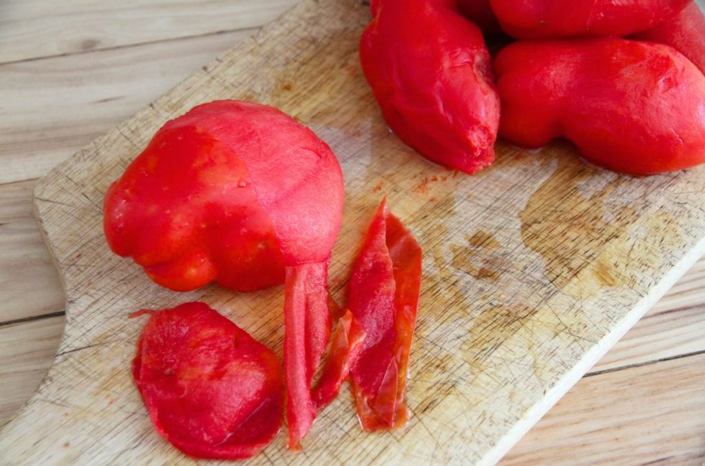 A cutting board with peeled tomatoes and tomato peels scattered about.