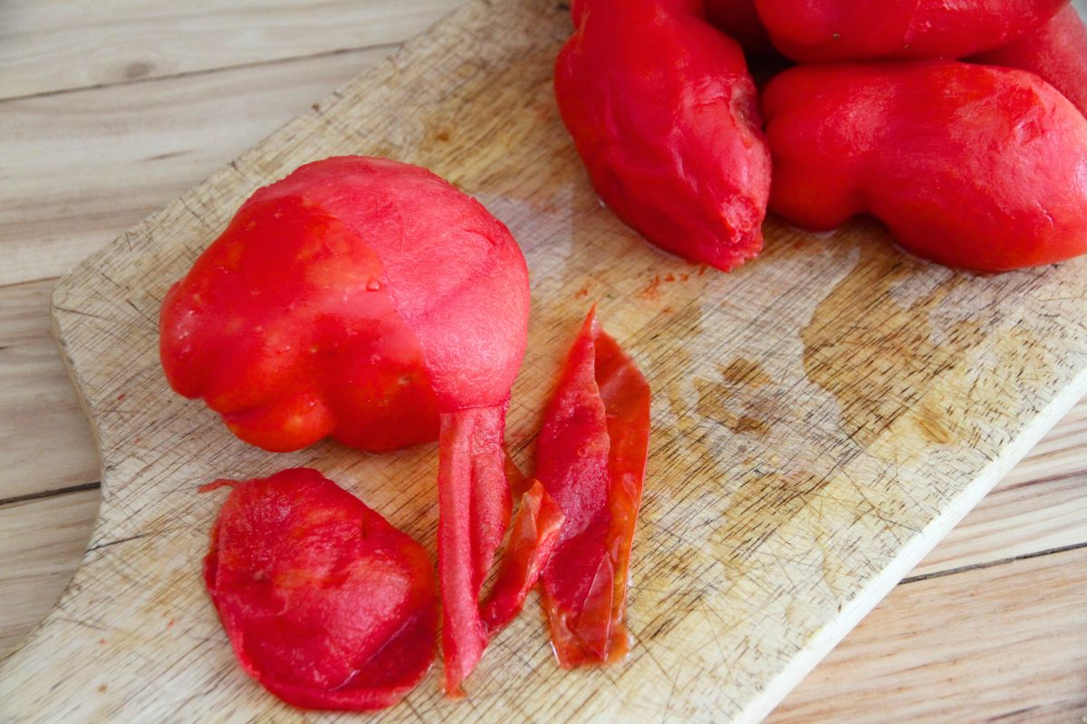 A cutting board with peeled tomatoes and tomato peels scattered about.