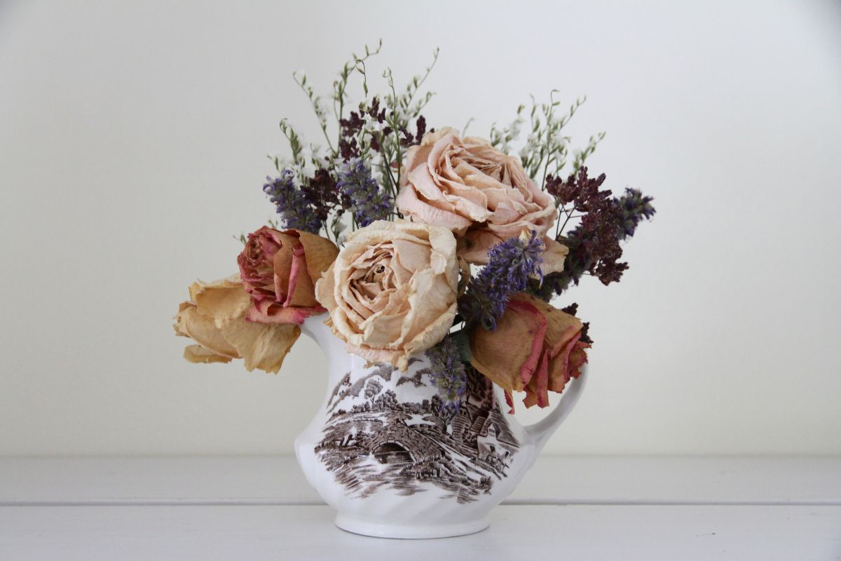 A small brown and white transferware creamer with a short and full bouquet of light and dark pink roses, hyssop and veronica.