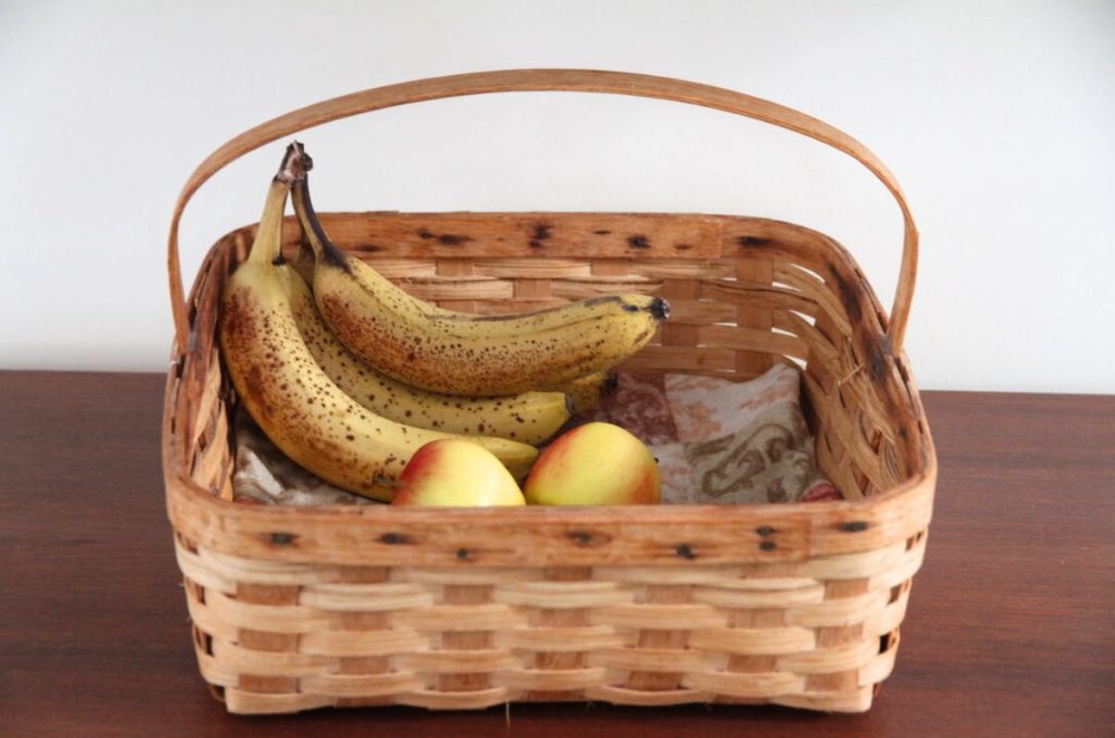 A square basket made from wood splits with a strong handle, holding fresh fruit.