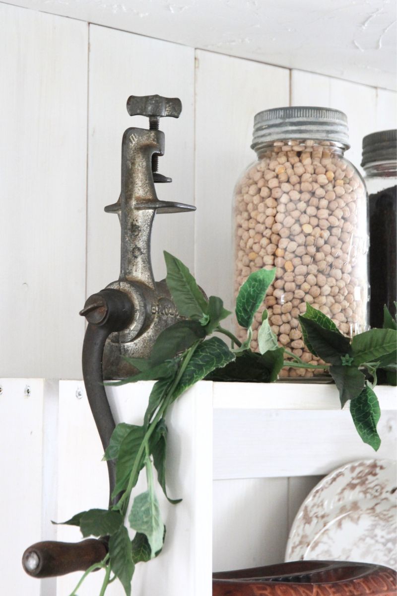 A silver, cast iron hand grinder sitting upside down on top of an open, kitchen shelf
