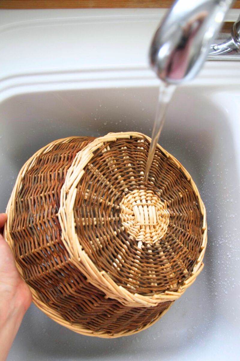 A wicker kitchen basket held under cold running water to remove dirt and dust.