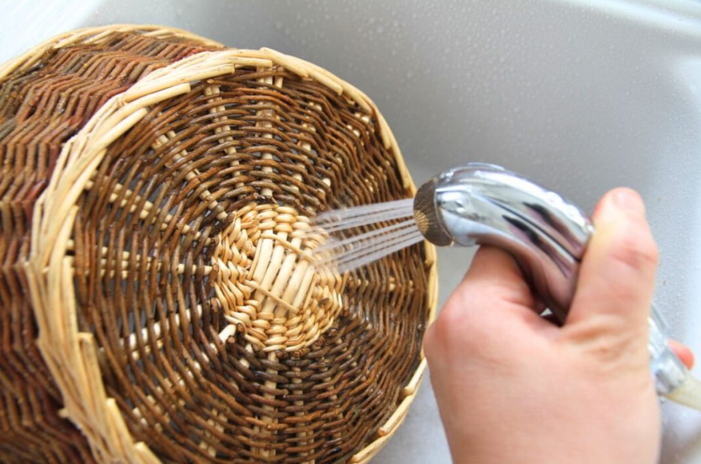 Spraying a hard wicker basket with a spray hose at the kitchen sink. 