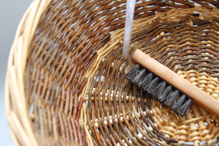 A woven wicker basket sitting under running water with a soft bristle brush.
