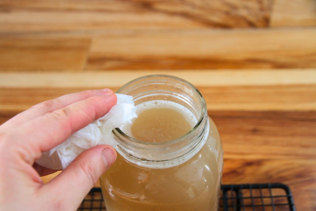 A jar of golden, hot broth being wiped with a paper towel.
