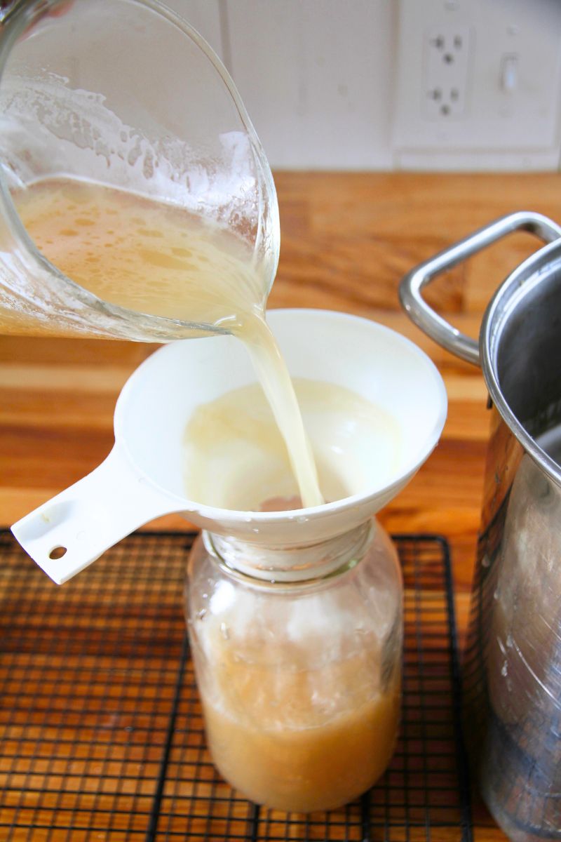Hot bone broth being poured into a glass jar with a white funnel at its mouth.