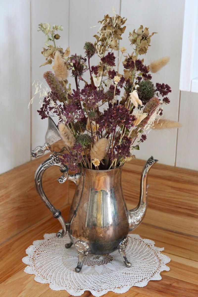 A silver teapot filled with dried herbs for a all-season floral arrangement