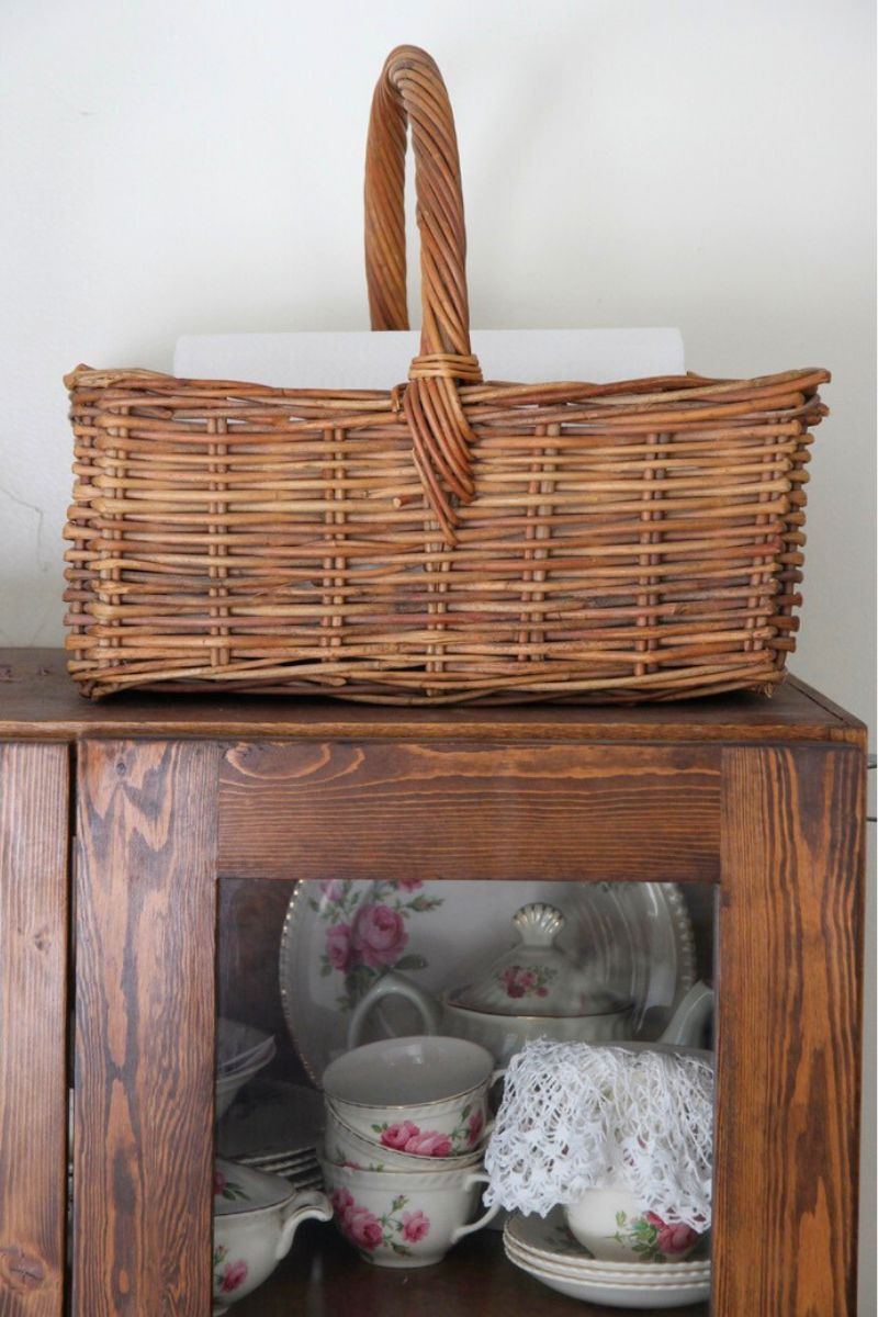 A square basket filled with paper towel, sitting on top of a kitchen hutch.