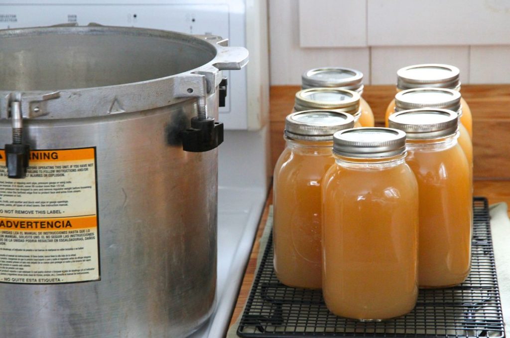 Seven quart jars of golden bone broth sitting next to a weighted gauge pressure canner.