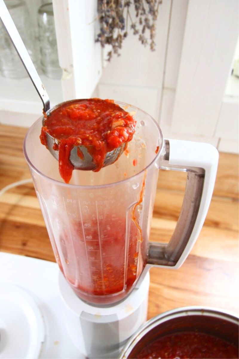 A mess of cooked tomatoes being ladled into a Bosch kitchen blender.