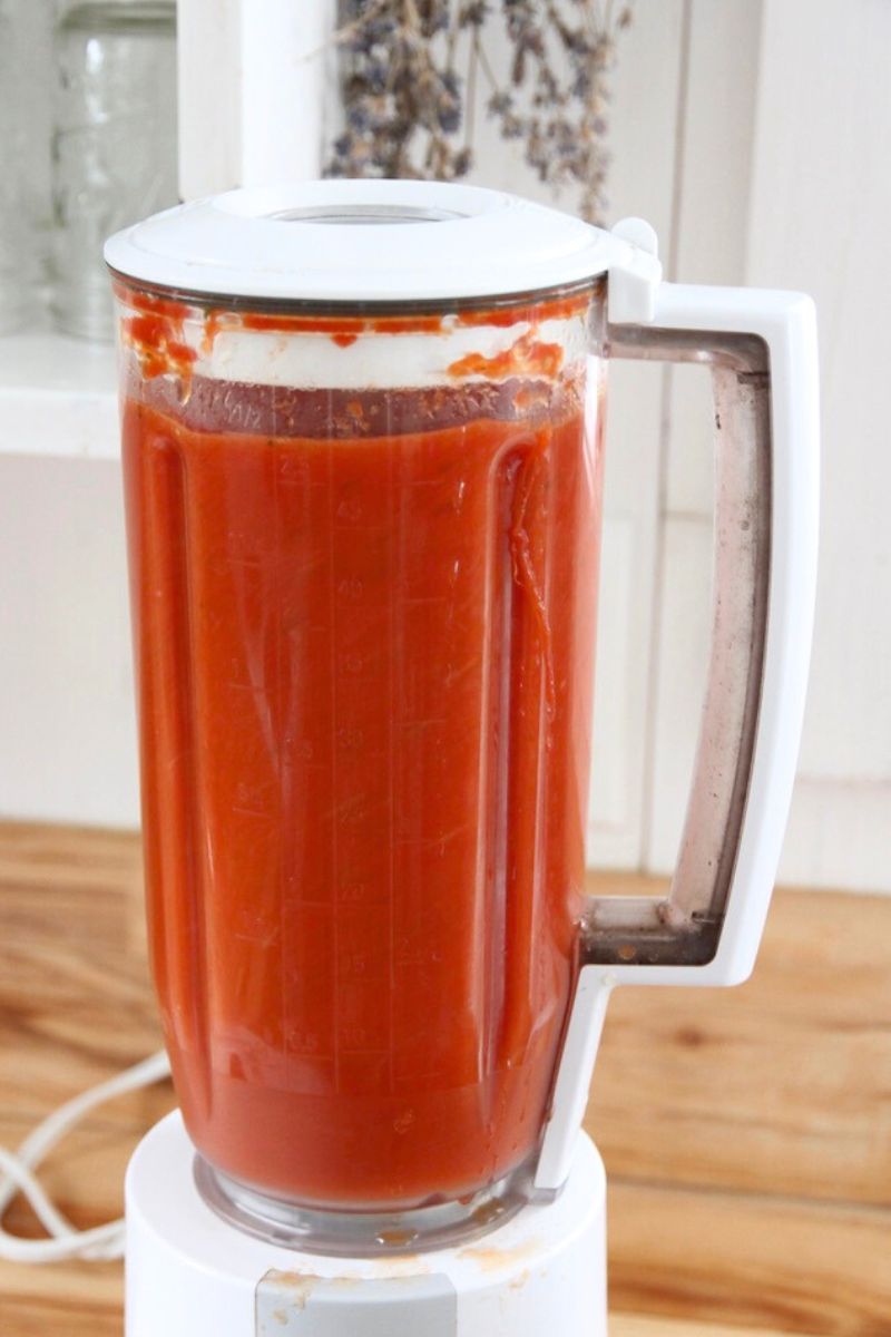 Pureeing cooked tomatoes in a kitchen blender for a thin sauce.