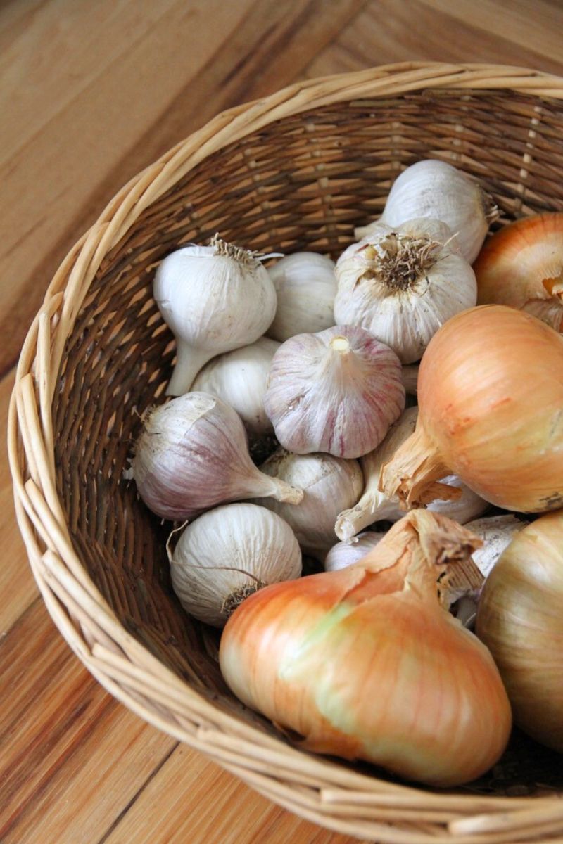 Onions and garlic in a round woven basket, sitting on a kitchen countertop.
