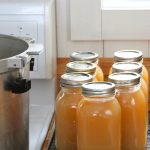 Jars of canned bone broth cooling on a rack while waiting for a seal.