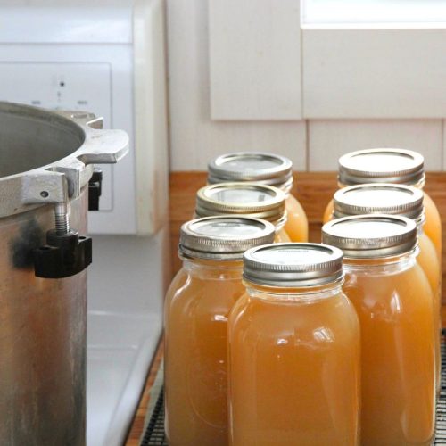 Jars of canned bone broth cooling on a rack while waiting for a seal.