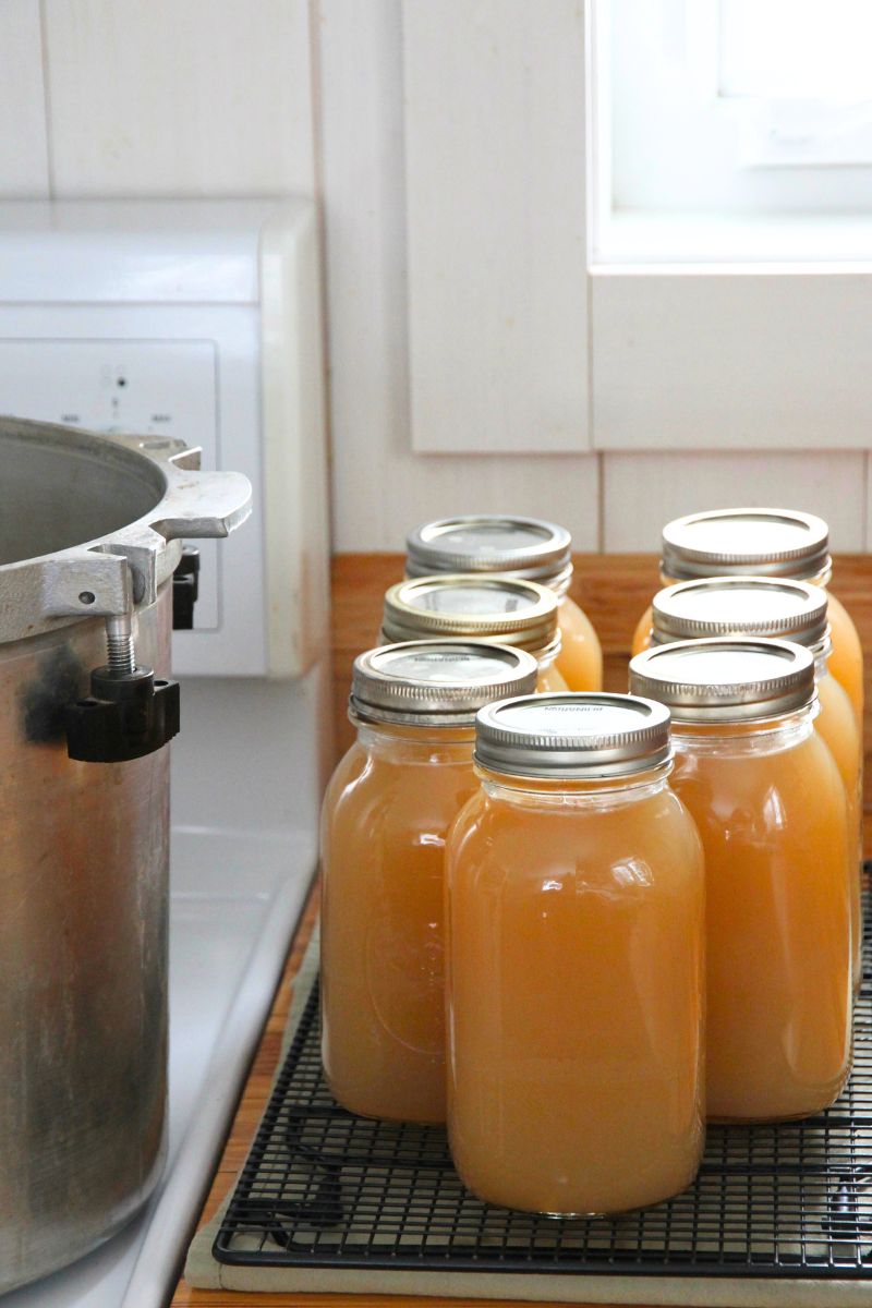 Jars of canned bone broth cooling on a rack while waiting for a seal.