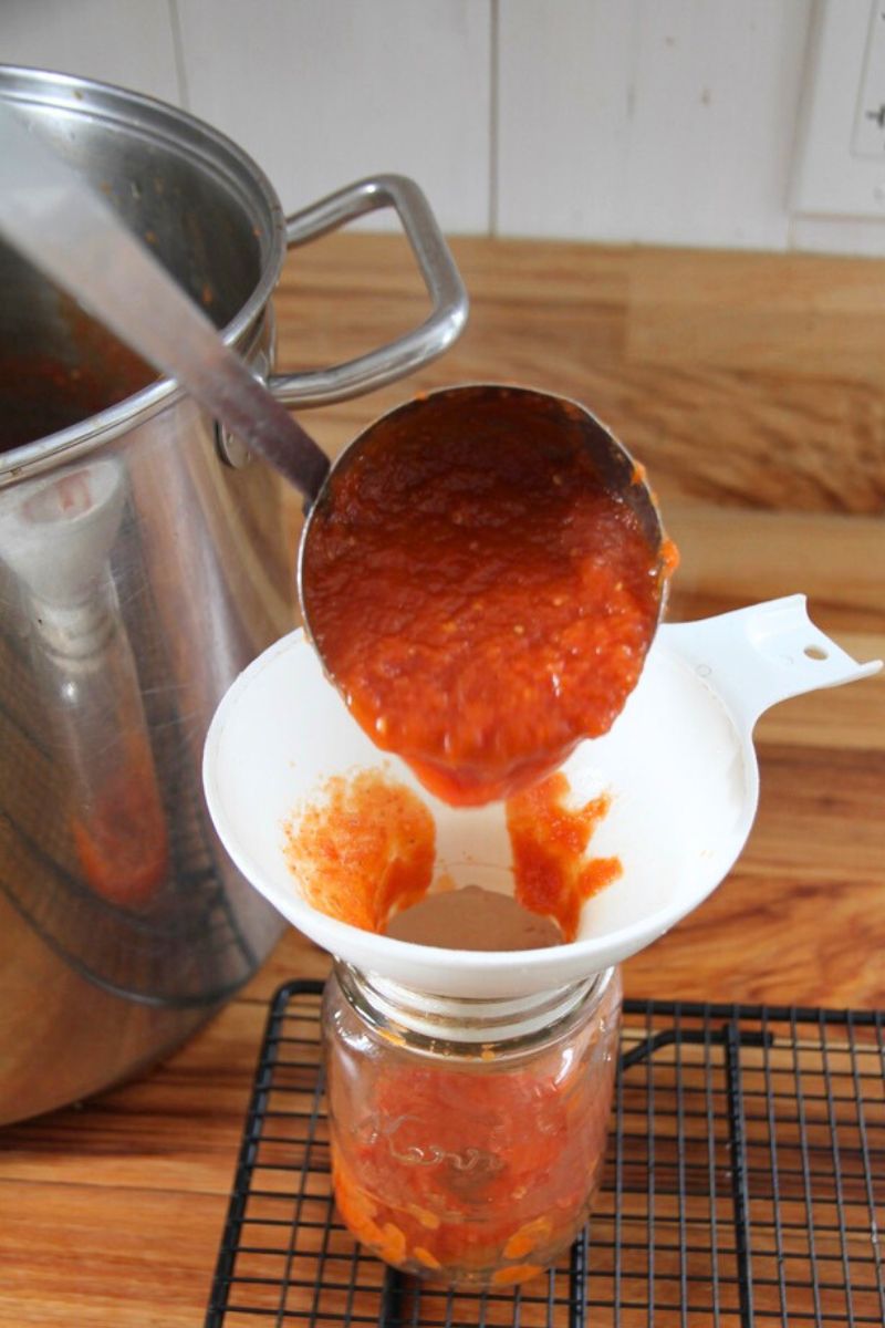 Ladling thick tomato sauce through a funnel into a pint jar.
