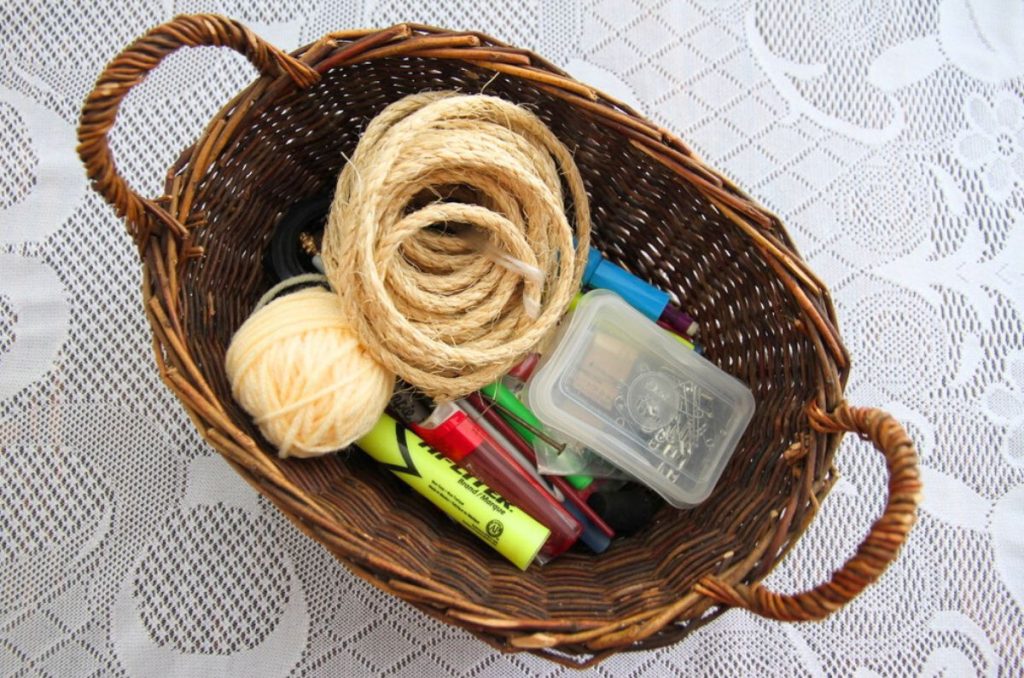A small oval basket filled with pens, pins, markers, twine, yarn and more.