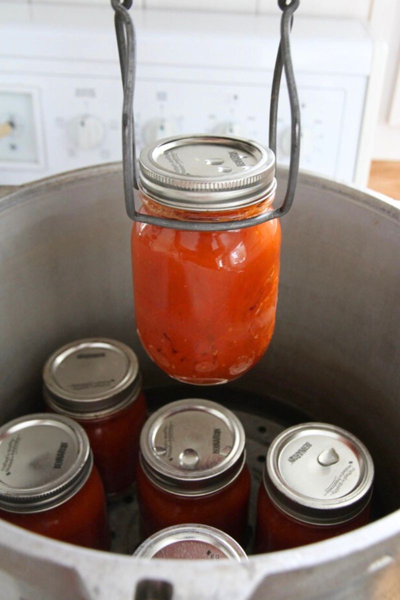 Hot jars of tomato sauce being removed from the pressure canner with a jar lifter.