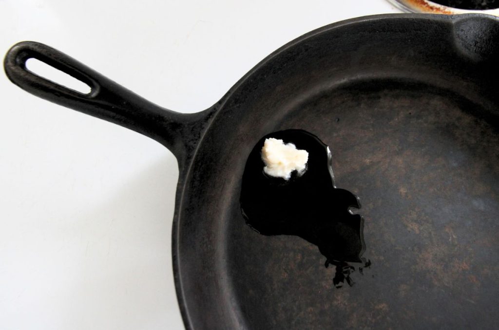 A spoonful of lard melting in a cast iron skillet on the stove top.