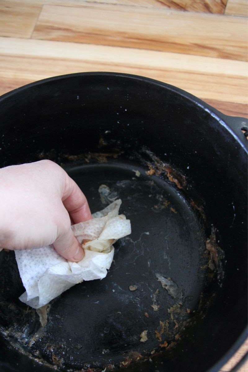 Wiping grease out of the bottom of a cast iron dutch oven with a dry paper towel