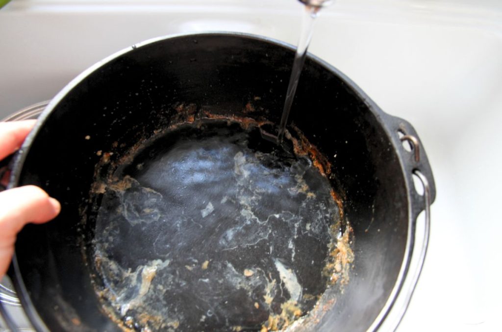 Adding water to a dutch oven that has food baked onto the sides and bottom of the pan.