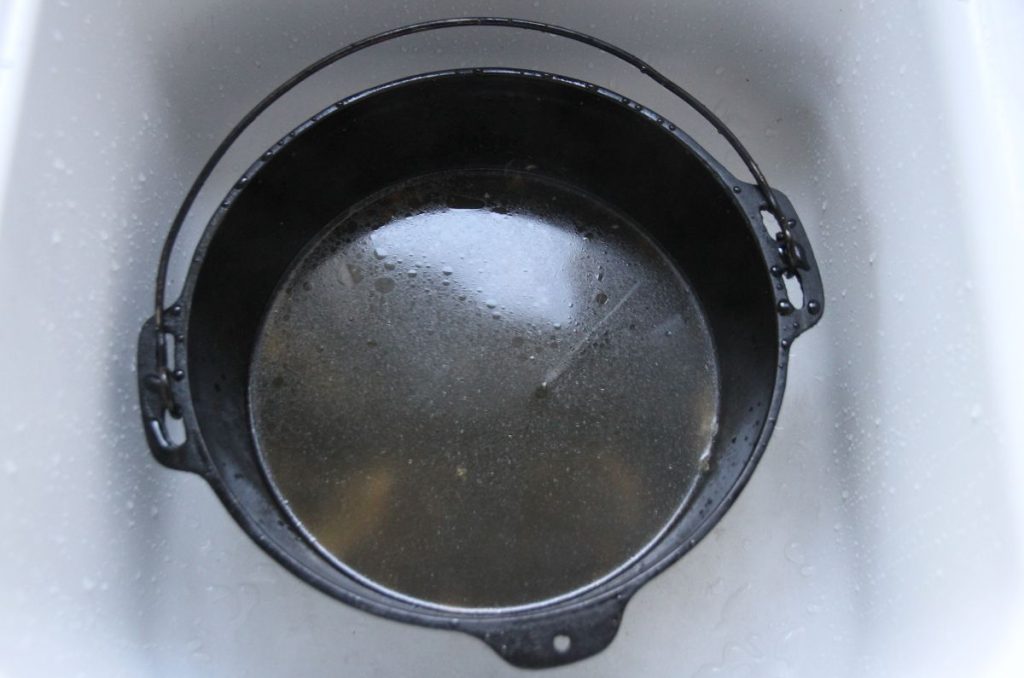 A hot cast iron dutch oven in the kitchen sink, with softened food bits on the inside.