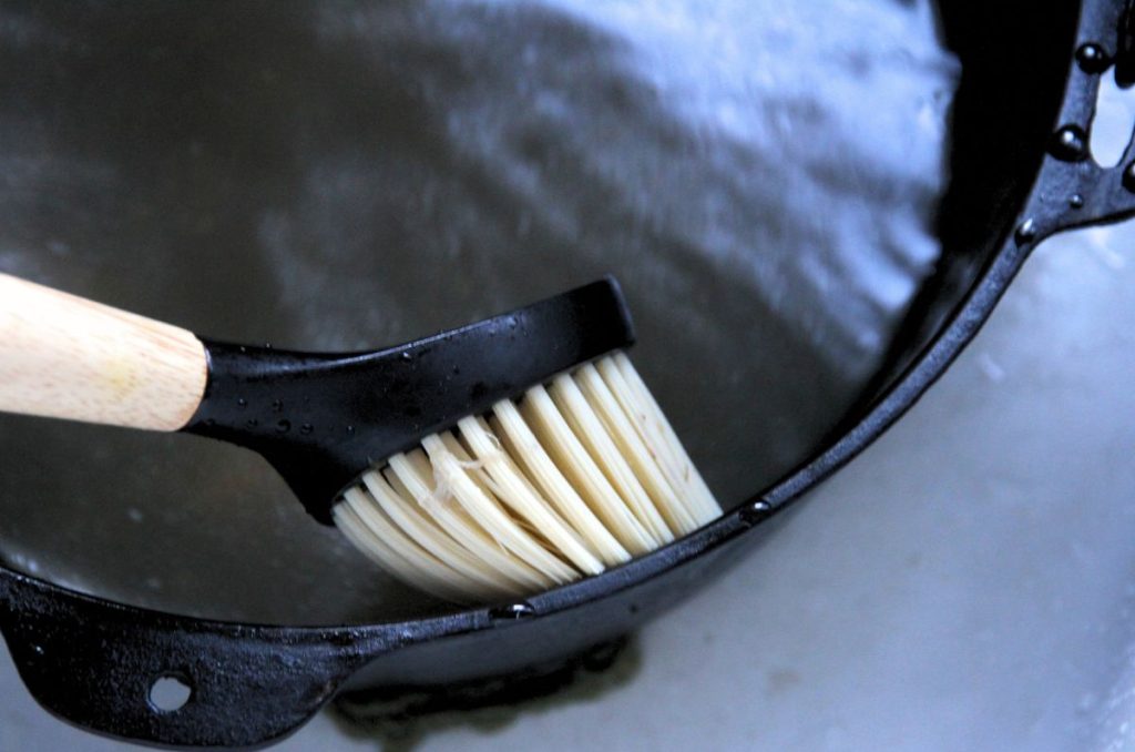 A scrub brush cleaning a cast iron dutch oven filled with boiling water