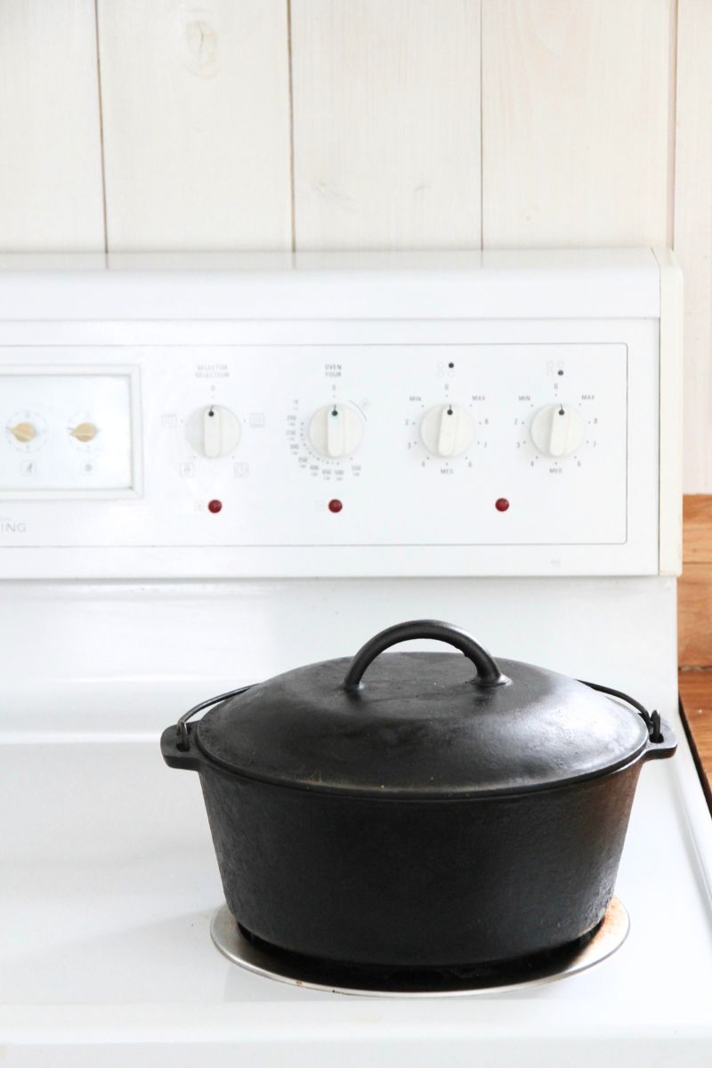 A black, cast iron dutch oven with a lid sitting on a white stove top.