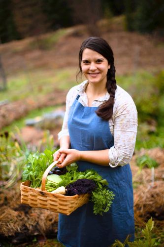 Image of a woman in a blue apron holding a basket in her garden