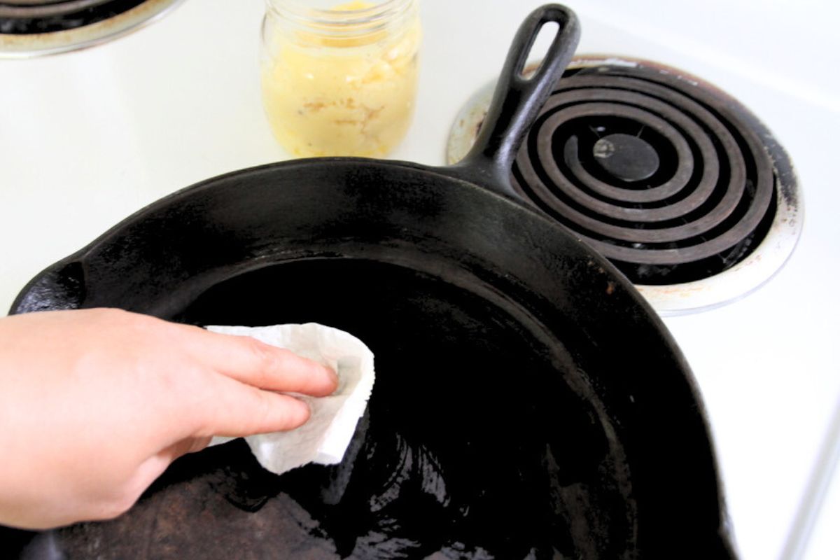 Wiping a warm cast iron skillet with paper towel and tallow fat.