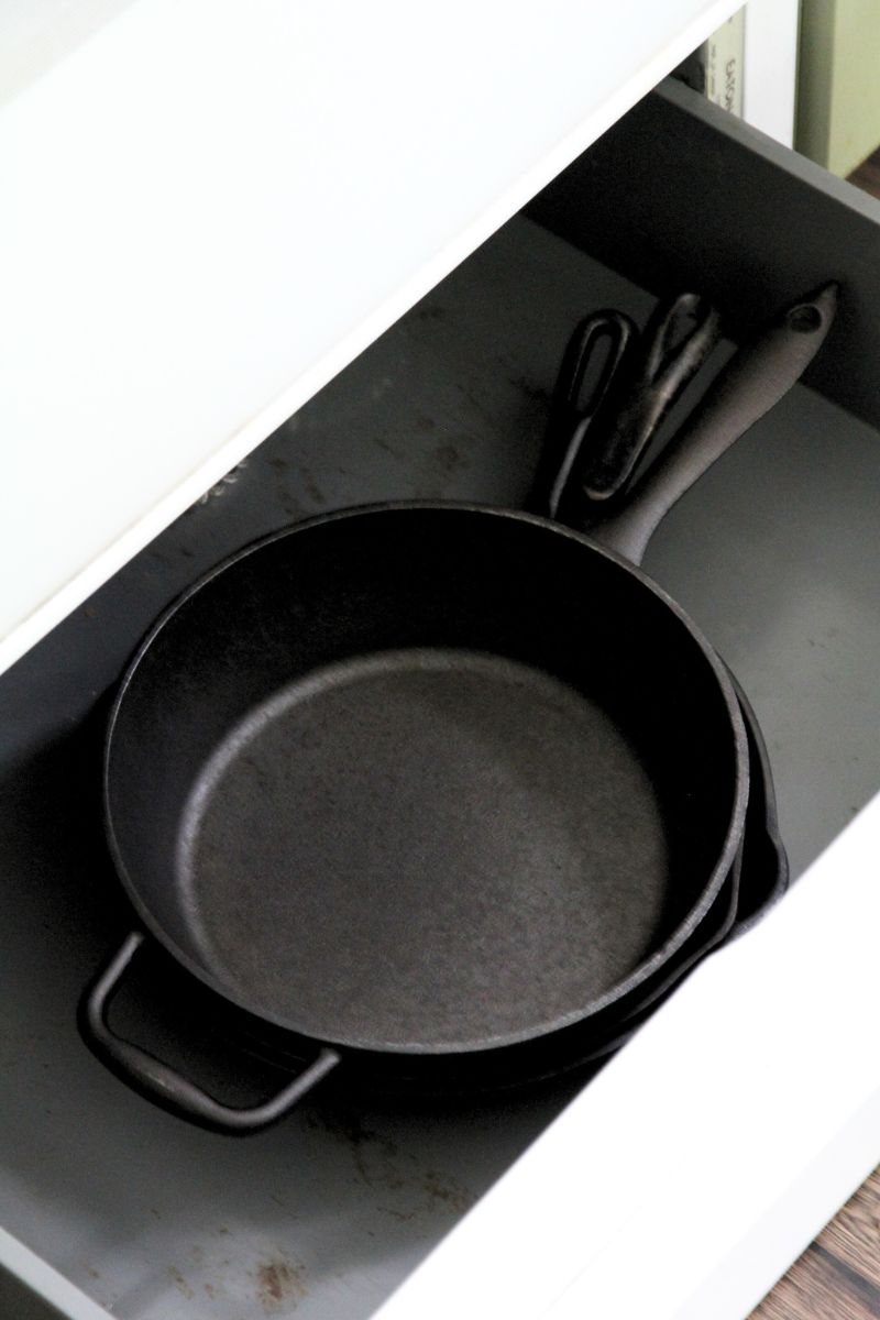 A stack of cast iron skillets in the metal drawer below the kitchen stove.
