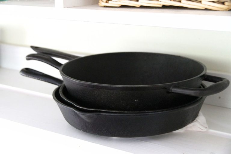 A stack of cast iron skillets on a white wooden shelf.