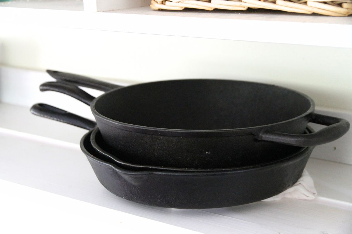 A stack of cast iron skillets on a white wooden shelf.