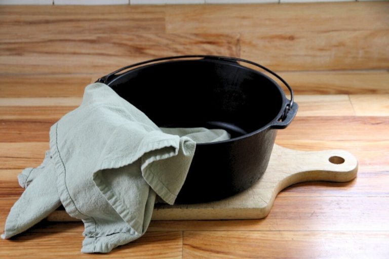 A cast iron skillet on a wood cutting board being dried with a green tea towel.
