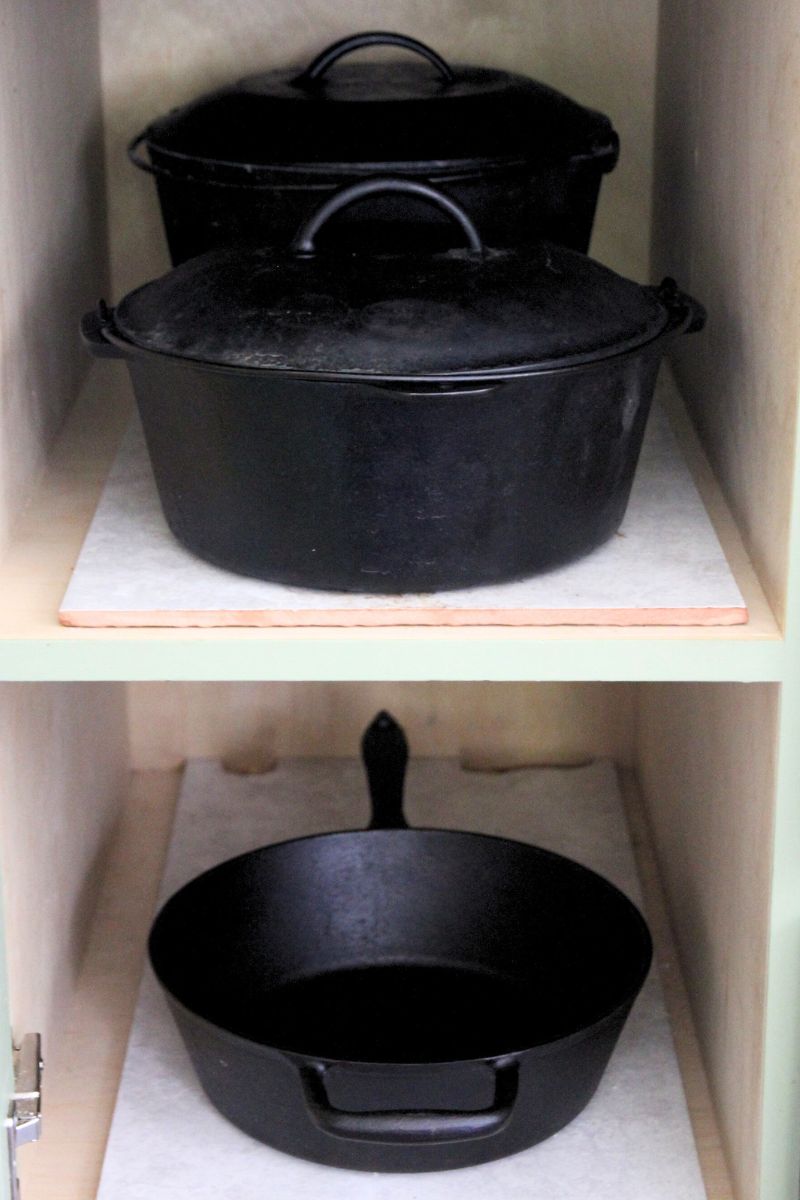 Cast iron dutch ovens and a deep skillet stacked on tile inside a kitchen cupboard.