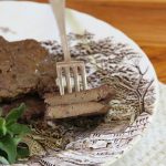 Freshly fried beef liver on a brown and white dinner plate with a side garnish of fresh herbs.