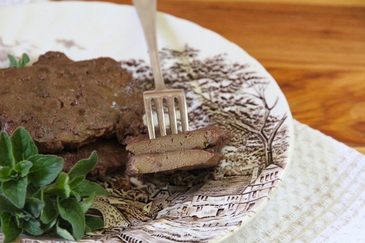 Freshly fried beef liver on a brown and white dinner plate with a side garnish of fresh herbs.